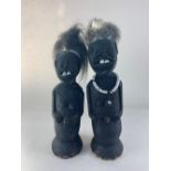 A pair of African black stained softwood figures, each with two buck teeth, one wearing a beaded