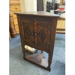 An oak corner cabinet on stand, with two carved panel doors, and triangular undershelf, on shaped