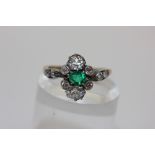 An emerald and diamond cluster ring claw set with an oval cut emerald within claw and collect set