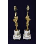 A pair of gilt metal figural table lamps, modelled as cherubs standing on white stone column
