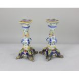 A pair of French faience candlesticks, decorated with flowers, on outswept feet, 24cm high