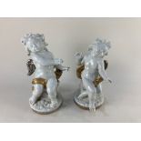 A pair of modern white ceramic cherubs with silver coloured wings, one seated on a barrel. the other