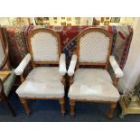 A pair of upholstered elbow chairs with padded backs and arms on turned supports and legs with