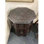 An Eastern carved octagonal side table with floral decorated removable top on folding base with