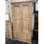 A pine wardrobe, with two panel doors enclosing a brass rail, and two drawers below, on bracket