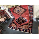 A Turkish wool carpet the central geometric motifs within floral border, on red ground 154cm by