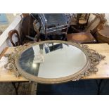 A giltwood and gesso oval wall mirror with cartouche and scroll surmount and foliate border, glass