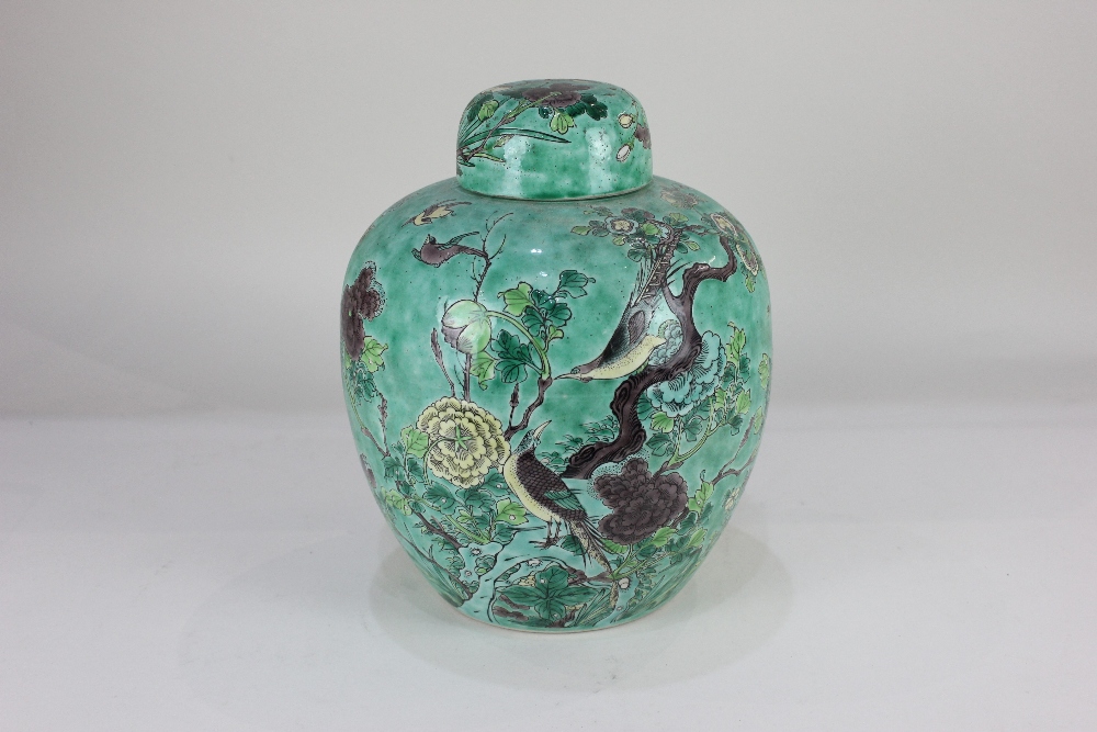 A porcelain ginger jar and cover, decorated with birds amongst flowering branches, on green