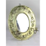 A brass oval wall mirror, with embossed floral decoration and two sconces, frame 42cm by 35cm