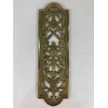 A pierced brass door finger plate, the central torch design within scrolling ribbon and floral
