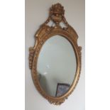 A gilt framed oval wall mirror with urn surmount, 54cm wide