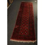 A Tekke style Afghan madder red ground strip runner, with two rows of guls within multiple