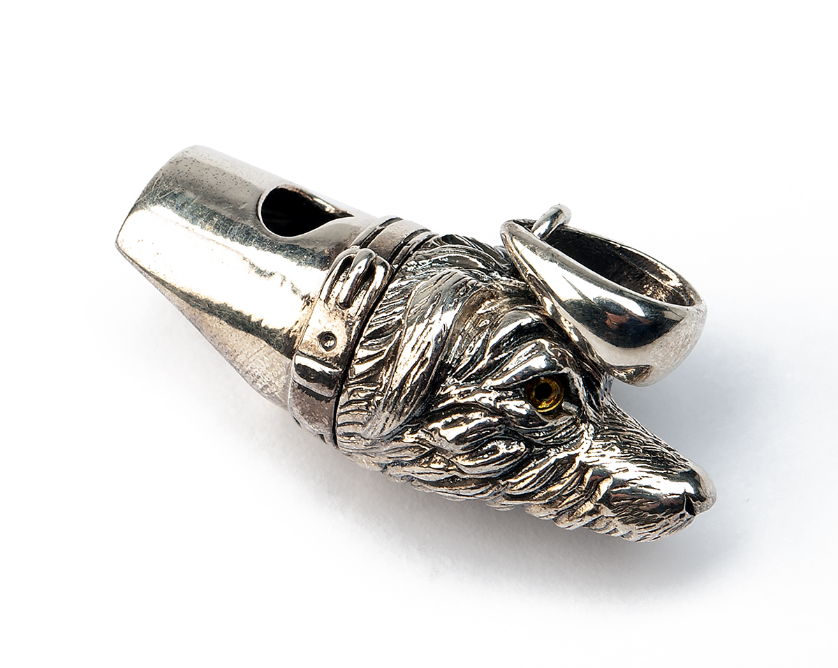 A STERLING SILVER DOG WHISTLE, marked 'STERLING', with glass eyes and lanyard ring, measuring