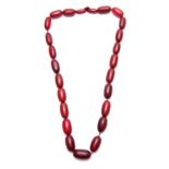 A RED STAINED HORN GRADUATED STRING OF ELONGATED ROUNDED BEADS 64cm overall