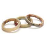 THREE CHINESE RUST JADE BANGLES 92mm, 93mm and 90mm diameter overall.