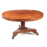 A REGENCY PLUM PUDDING MAHOGANY CENTRE TABLE with wide cross-banded tilt top; standing on a ring