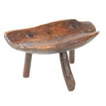 AN EARLY PRIMITIVE WALNUT MILKING STOOL with dished seat, standing on three branch legs 41cm wide