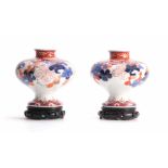 AN UNUSUAL PAIR OF 19TH CENTURY SQUAT BULBOUS FOOTED IMARI VASES ON HARDWOOD STANDS colourfully