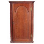 AN EARLY 18TH CENTURY OAK HANGING CORNER CUPBOARD with arched fielded panelled door, the interior