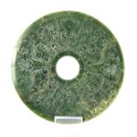 A CHINESE SHALLOW CARVED SPINACH JADE PI decorated on both sides with a stylised ox and various