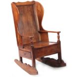 AN 18th CENTURY ELM LAMBING CHAIR with shaped back and headrest above open arms with panelled seat