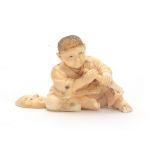 A JAPANESE CARVED IVORY OKIMONO modelled as a young seated boy holding a chisel making a Noh mask