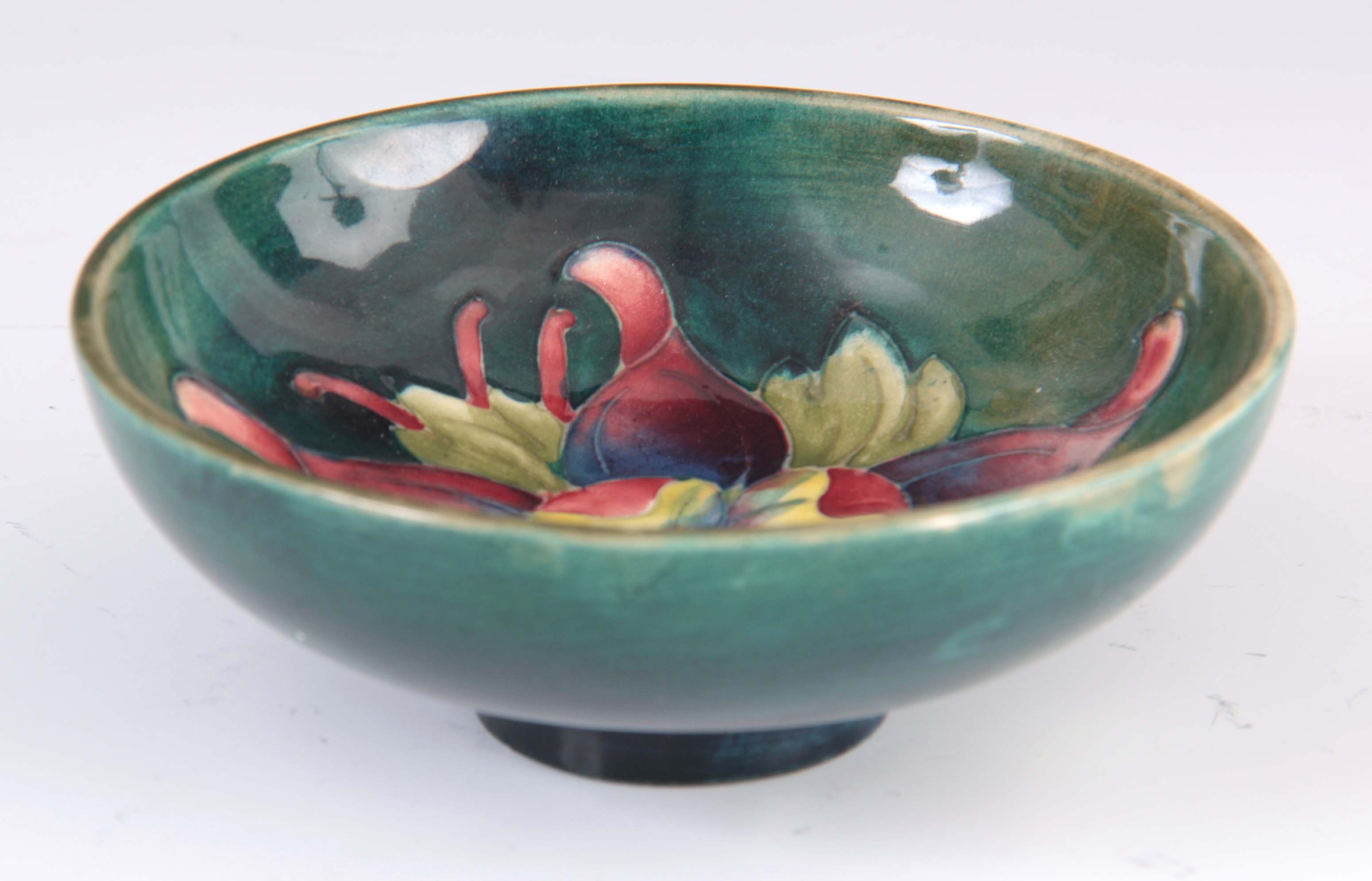 A CIRCA 1950S WALTER MOORCROFT COLUMBINE PATTERN FOOTED BOWL on a green ground 4cm high, 11.5 cm