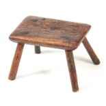 AN 18TH CENTURY OAK MILKING STOOL with thick-cut chamfered top, having traces of original green