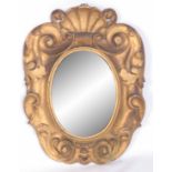 A LATE 18th CENTURY GILTWOOD OVAL MIRROR, the scrollwork frame with scollop shell pediment and