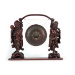 AN EARLY 20th CENTURY CHINESE HARDWOOD FIGURAL GONG having two oriental figure supports 51.5cm high,