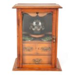 A STYLISH EDWARDIAN OAK SMOKERS CABINET with glazed door enclosing a shelved three drawer interior