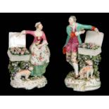 A PAIR OF DERBY FLOWER SELLER FIGURE GROUPS WITH DOGS each dressed in classical costume displaying