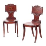 A PAIR OF REGENCY MAHOGANY HALL CHAIRS with scrolled carved backs having painted coats of arm to the