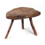 AN EARLY PRIMITIVE ELM STOOL with a thick-cut triangular top; raised on stick legs 43cm wide 36cm