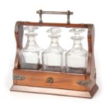 A 19TH CENTURY WALNUT THREE BOTTLE SPIRIT TANTALUS with silver plate strapwork mounts and bar handle
