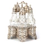 A GEORGE III SILVER TABLE CRUET SET comprising five cut glass bottles mounted in a pierced shaped