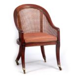 A REGENCY MAHOGANY BERGERE LIBRARY CHAIR with an arched roll-over canework back and seat, covered