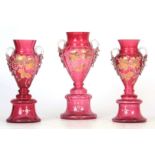 A GARNITURE OF THREE VICTORIAN CRANBERRY VASES each of two-handled pedestal form with white enamel