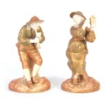 A PAIR OF ROYAL WORCESTER IVORY GROUND AND GILT EDGED COLOURED FIGURES modelled as Boy Piper and