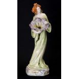 AN ART NOUVEAU GLAZED POTTERY FIGURE modelled as a standing lady clutching a flower head with hollow