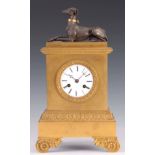AN EARLY 19TH CENTURY FRENCH ORMOLU MANTEL CLOCK surmounted by a patinated recumbent greyhound