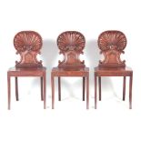 A SET OF THREE REGENCY HALL CHAIRS IN THE MANNER OF GILLOWS with shell carved and scrolled backs