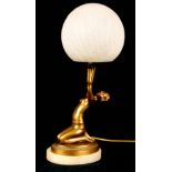 AN ART DECO GILT METAL TABLE LAMP depicting a seated nude female holding a crackle-glazed glass