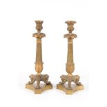 A PAIR OF REGENCY BRASS CANDLESTICKS with tapering reeded stems, leaf cast scones, and standing on