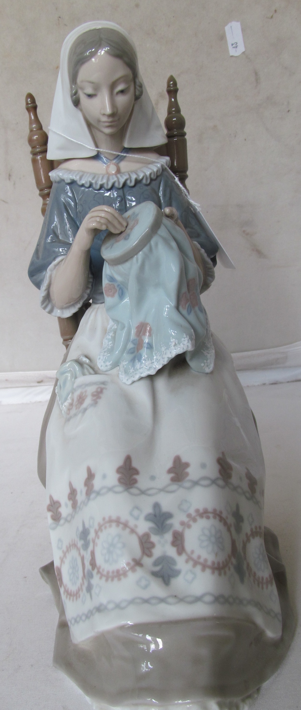 A Lladro figure lady seated in a chair sewing