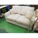 A beige upholstered two seater bed settee