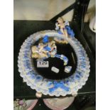 A freestanding porcelain blue and white oval mirror with two cherubs (both a/f)