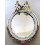 A Dresden style oval mirror with two cherubs holding garland to top