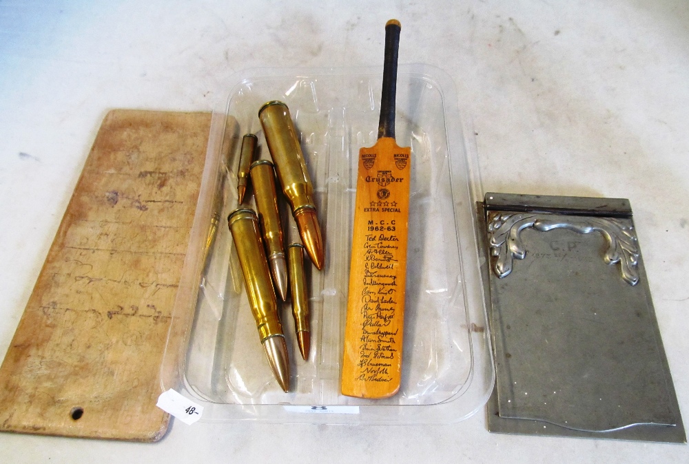 Five brass bullet cases, a metal notebook holder marked C.P. 1873 28/9 - 1933, a wooden board and an