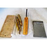 Five brass bullet cases, a metal notebook holder marked C.P. 1873 28/9 - 1933, a wooden board and an